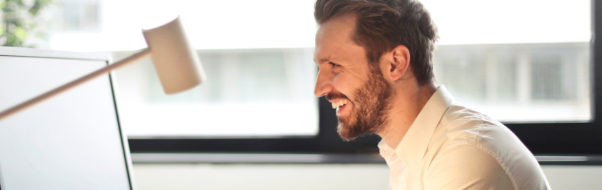 Homme souriant concentré devant son ordinateur dans son bureau, illustrant le poste de DSI et le travail quotidien